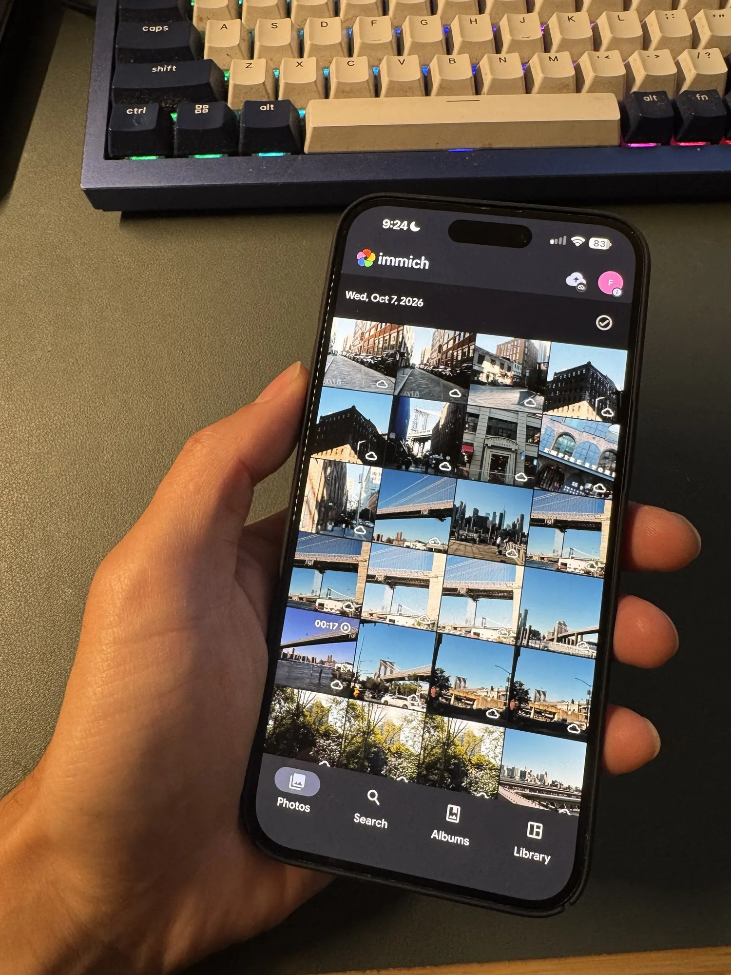 An iPhone showing the Immich app's photo timeline, with backed-up street and bridge shots and a 17-second video.